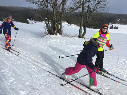 Zwei Schülerinnen auf Langlaufskiern üben mit ihrer Betreuerin den Diagonalschritt.