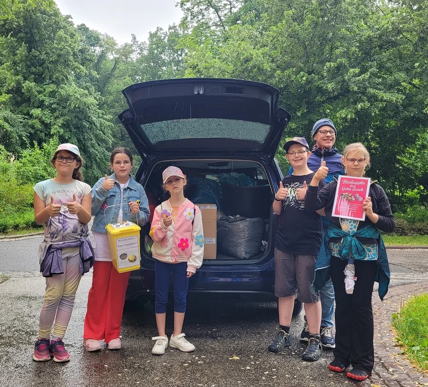 Sechs Schülerinnen und Schüler stehen vor einem Auto, in dem viele große Säcke mit Kronkorken verstaut sind. Die Kinder halten ihre Daumen in die Höhe.