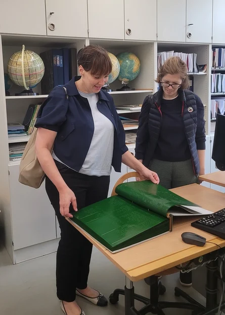 Zwei Frauen stehen an einem Tisch. Darauf liegt ein großes Buch mit Brailleschrift, das sie sich anschauen.