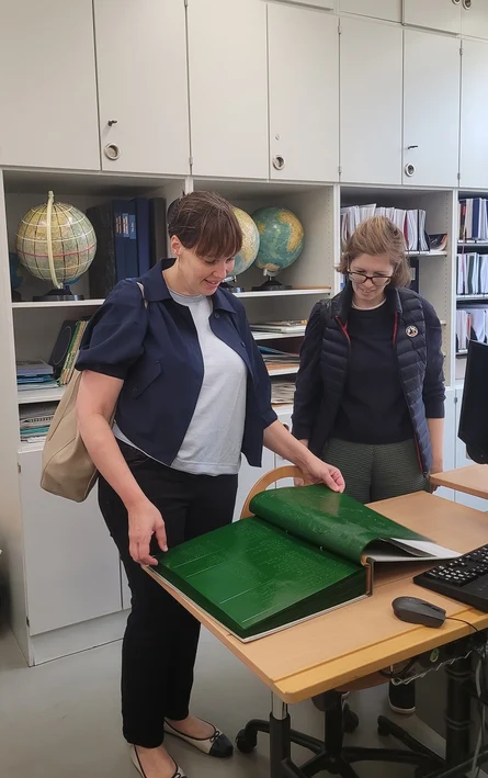 Zwei Frauen stehen an einem Tisch. Darauf liegt ein großes Buch mit Brailleschrift, das sie sich anschauen.