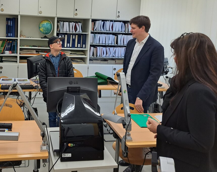 Herr Clemens steht mit Frau Saborowski in einem Klassenzimmer und unterhält sich mit einem Schüler
