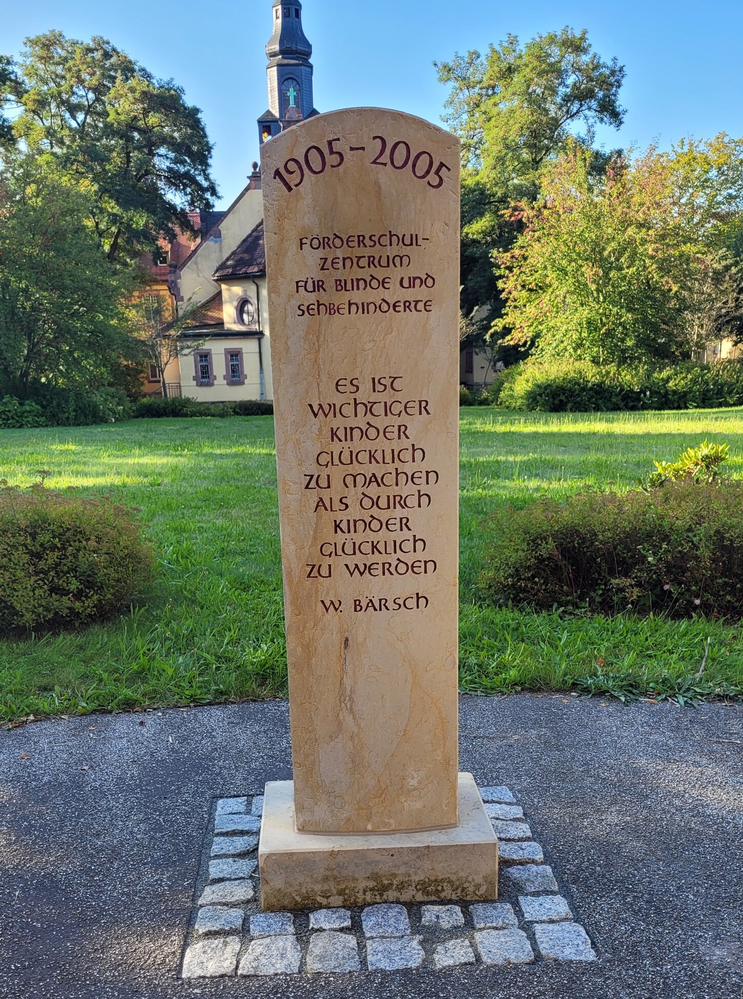 Ein hoher Stein, auf dem die Jahreszahlen 1905 bis 2005, der Schulname sowie der ein Zitat eingraviert sind.