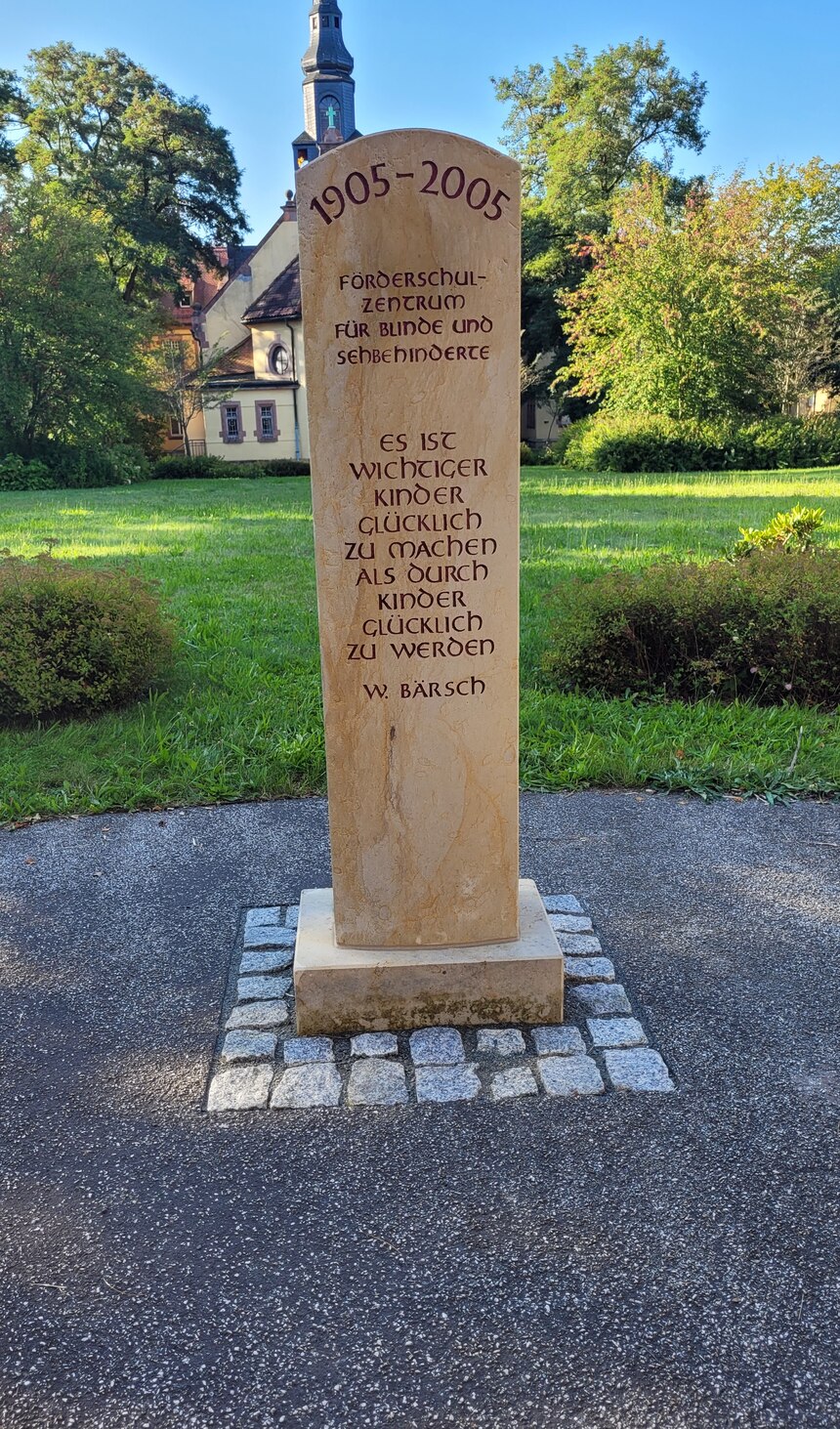 Ein hoher Stein, auf dem die Jahreszahlen 1905 bis 2005, der Schulname sowie der ein Zitat eingraviert sind.
