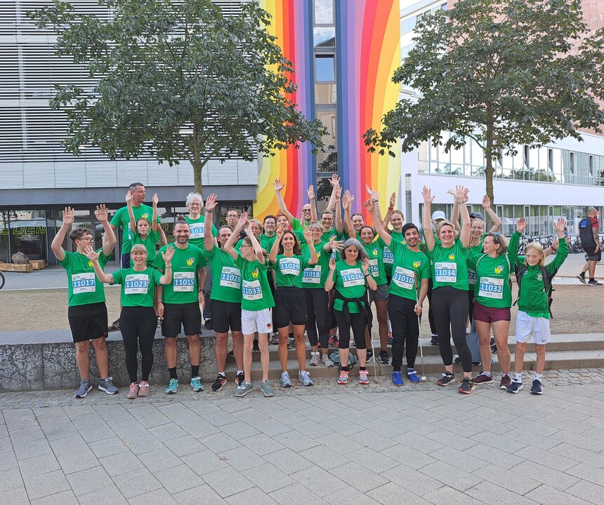 Lehrkräfte, Mitarbeiter und Schüler der Landesschule stehen vor einem bunt bemaltem Gebäude und jubeln mit hochgehaltenden Armen. Sie tragen alle das gleiche T-shirt.