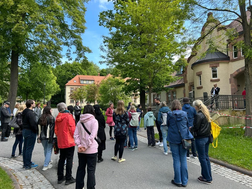 Eine Gruppe von Menschen steht auf dem Gelände der Landesschule und hört einem Redner zu.