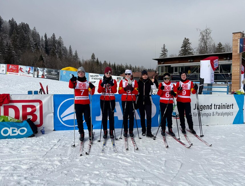 Unsere Mannschaft steht auf Langlaufski mit ihrer Lehrerin im Schnee und zeigen den Daumen nach oben.