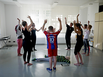 Mehrere Tänzer stehen mit nach oben gestreckten Armen im Kreis. In der Mitte liegt ein Schüler auf dem Boden.