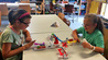 Zwei Mädchen aus der Klasse 5 sitzen sich am Tisch gegenüber und probieren im Spielemuseum ein Spiel aus.