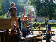 Beim Wasserspielplatz spritzt ein Junge seine Mitschüler nass.