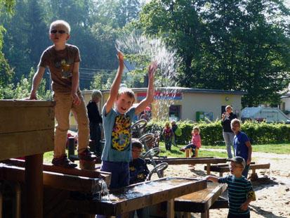 Beim Wasserspielplatz spritzt ein Junge seine Mitschüler nass.