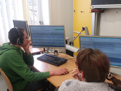 Zwei Schüler mit Kopfhörern sitzen am Computer und bearbeiten die aufgenommenen Audiodateien mithilfe des Computerprogramms Audacity.