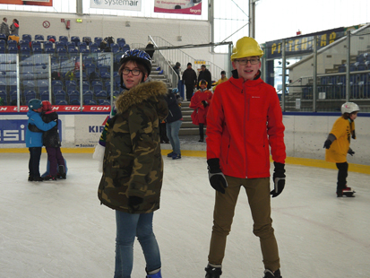 Im Vordergrund sind zwei ältere Schüler aus der Klasse 9 zu sehen, die offensichtlich viel Spaß beim Eislaufen haben.