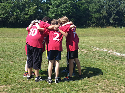 Alle Spieler unserer Mannschaft stehen vor dem Spiel eng umarmt im Kreis auf dem Fußballfeld und motivieren sich gegenseitig.
