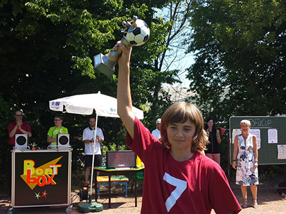 Ben geht zur Mannschaft unserer Schule und trägt stolz den Pokal in der rechten Hand und hält ihn gestreckt nach oben. Alle Anwesenden klatschen Beifall für unsere Mannschaft.