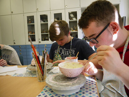 Das Bild zeigt zwei Schüler beim Glasieren ihrer gebrannten Keramik-Schüsseln.