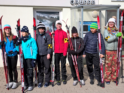 Sieben junge Sportler stehen mit ihren Langläufern in freudiger Erwartung vor der Skihalle.