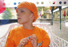 Junge mit orangem T-Shirt und Kopftuch vor einer Fensterscheibe mit Blick nach draußen