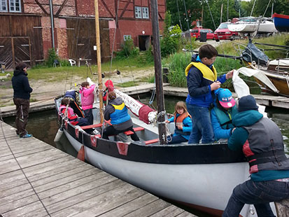 Acht Schüler sind am und auf dem Segelboot und bereiten alles für das Abfahren los.