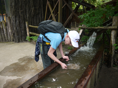 Ein Schüler, der vor einer Wasserrinne steht, sucht mit einem Sieb nach Gold und Edelsteinen.