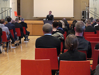 Herr Kretschmer steht am Rednerpult vor der Bühne im Haus 4. Viele Menschen sitzen in Stuhlreihen und hören zu.