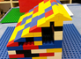 Ein Schüler baut ein Gebäude aus bunten Legosteinen. Markant ist eine lange Außentreppe entlang des ganzen Gebäudes.