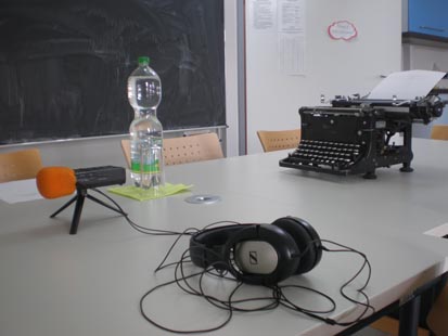 Das Bild zeigt die Vorbereitungen auf das Interview. Ein Aufnahmegerät, ein Getränk für den Zeitzeugen sowie eine alte Schreibmaschine von Wanderer stehen auf einem Tisch bereit.