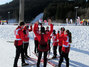 Alle Sportler haben mit ihren Langläufern im Schnee einen Kreis gebildet und reißen ihre Arme beim Schlachtruf hoch.