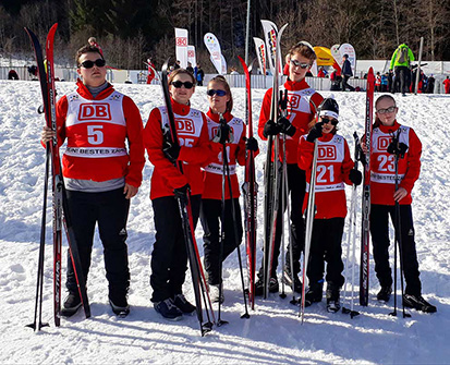Unsere 6 Sportler stehen im Schnee mit Wettkamfpbekleidung und Skiern nebeneinander an der Langlaufstrecke.