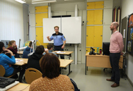 Ein Polizist steht im Klassenzimmer vor den Schülern und erklärt mit starker Gestik den Sachverhalt.