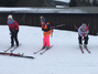 Drei Schülerinnen üben vor dem Skifahren die Abwärtshocke im Stehen.