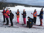 Acht Schüler auf ihren Skiern vor einer winterlichen Landschaft mit Feld und Wald im Hintergrund.