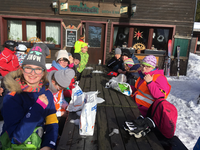 Sonnige Rast von allen Skischülern an einem großen Holztisch vor einer Gaststätte.