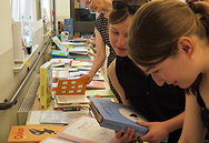 Zwei Schülerinnen und eine Lehrerin betrachten angeregt die Vielzahl an angebotenen Büchern auf dem Büchertisch der DZB lesen.