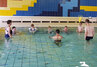 Alle Schüler stehen im Wasser am Beckenrand und hören aufmerksam den Erläuterungen der Schwimmtrainer zu.