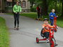Vier Schüler fahren voller Freude auf einem asphaltierten Weg mit Rollern, Dreirad und Pedalo.