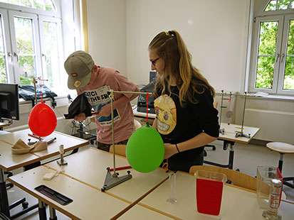 Jonas und Julia aus der 8. Klasse erklären interessante Physikexperimente mit farbigen Luftballons.