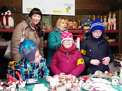 Die Schüler der Klasse M2 und zwei Betreuerinnen verkaufen im Weihnachtsstand. Vor ihnen stehen auf einem Verkaufstisch viele von unseren Schülern hergestellte Keramikarbeiten.