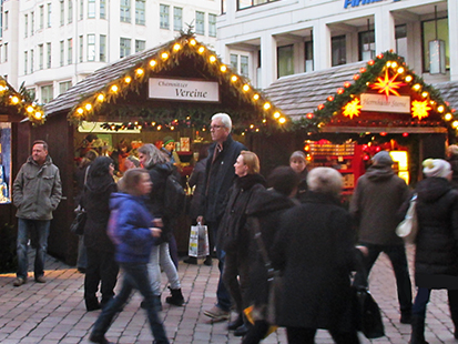 Auf diesem Bild sieht man 4 hübsch dekorierte Stände vom Chemnitzer Weihnachtsmarkt, vor dem viele Leute laufen. Der Stand 16 ist der von den Chemnitzer Vereinen, den wir kostenlos mieten konnten.