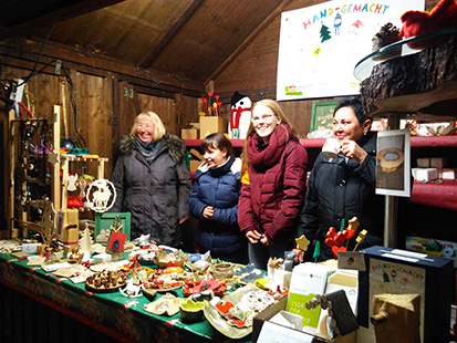 Olivia, Lena, Frau Schröter und Frau Schmidt stehen hinter dem Verkaufstand und preisen mit guter Laune am Abend unsere letzten „HAND-GEMACHT“ Dinge an.