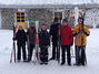 6 Kinder mit Ski in der Hand stehen vor der Skihütte.