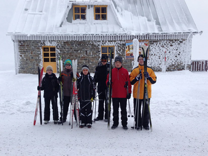 6 Kinder mit Ski in der Hand stehen vor der Skihütte.