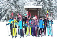 Eine Gruppe von Schülern steht mit ihren Langlaufskiern auf einer verschneiten Wiese und schaut in die Kamera.
