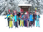 Eine Gruppe von Schuelern steht mit ihren Langlaufskiern auf einer verschneiten Wiese und schaut in die Kamera.