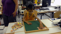 Ein sehbehinderter Grundschüler aus der Lernförderschule sitzt am Tisch und ordnet Symbole und verschiedene Mengen in einen Rahmen ein.