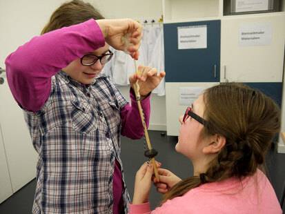 Zwei Schülerinnen spinnen mit einer Spindel Wolle zu Garn.