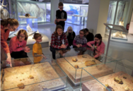 Schüler hocken mit der Museumspädagogin des »smac« um eine Glasvitrine. Darin befinden sich Ausgrabungsstücke.