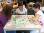 Drei Mädchen sitzen im Spielemuseum am Tisch und spielen das Spiel „Monopoly“.